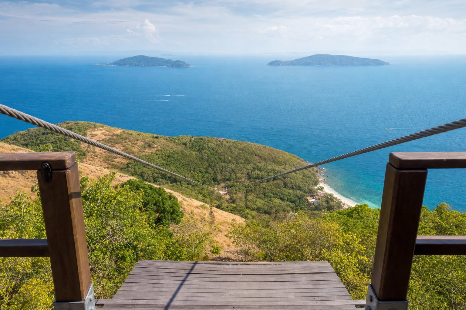 View from a coastal zipline platform across a wide ocean channel to two distant islands