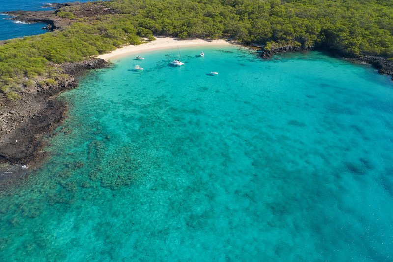 A sheltered tropical cove with turquoise shallow water, a pale sand beach and small boats at anchor